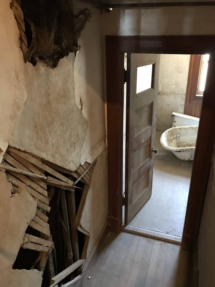 stairway down to a bathroom with demolished stair wall and broken bathtub