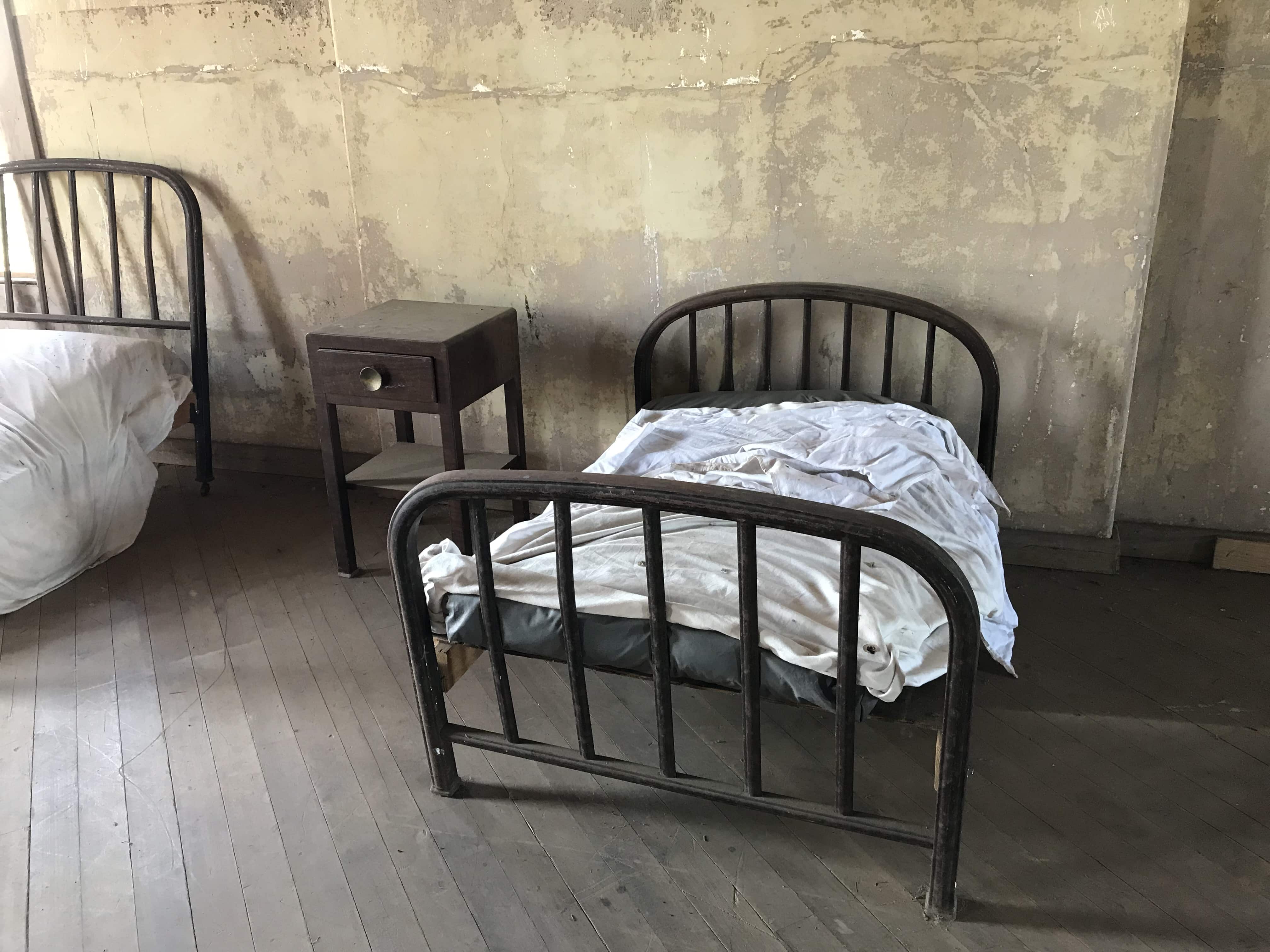 dirty black metal bed with thin white blanket and small side table