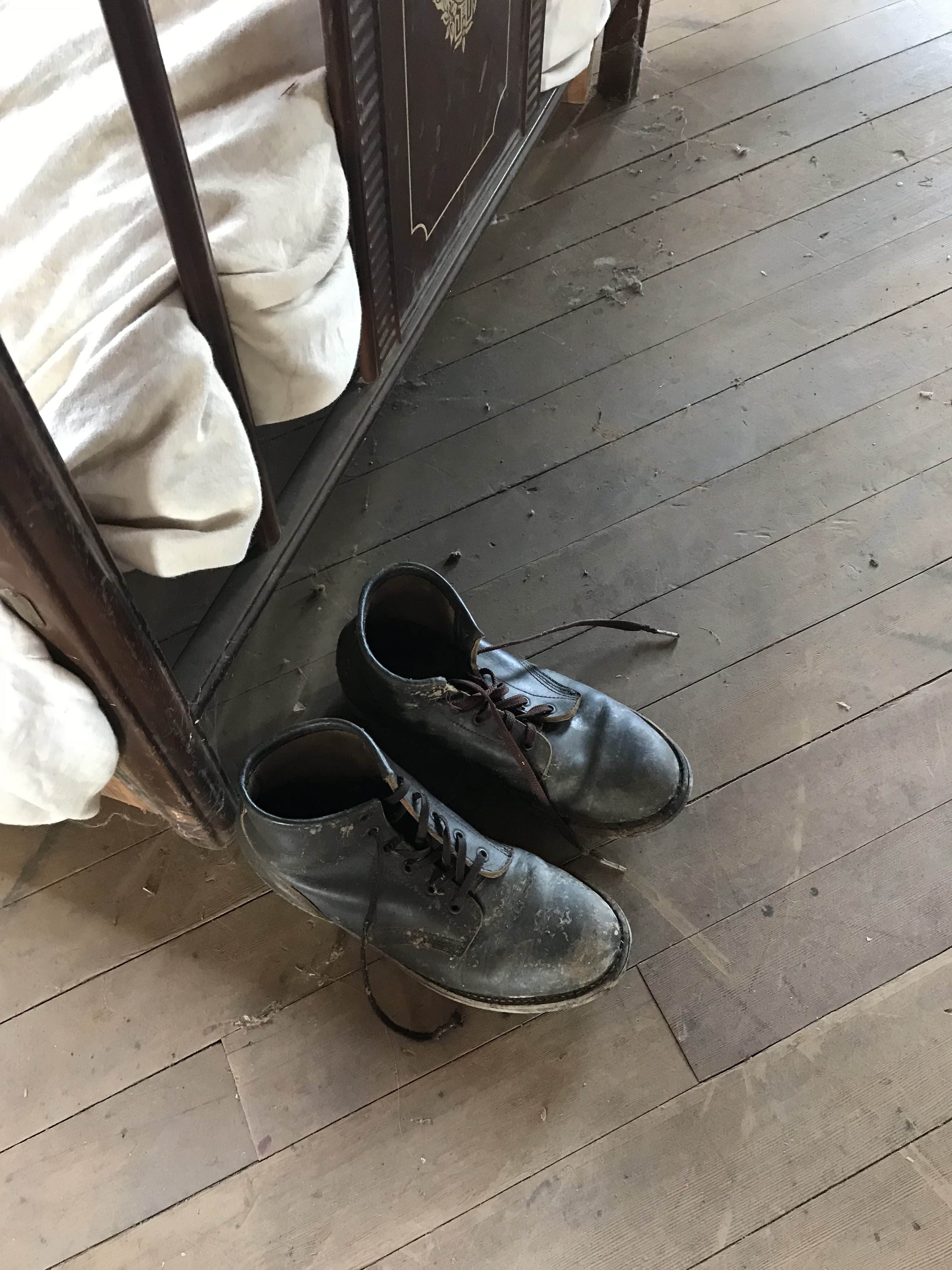 Pair of black shoes with untied laces at the foot of a metal bed