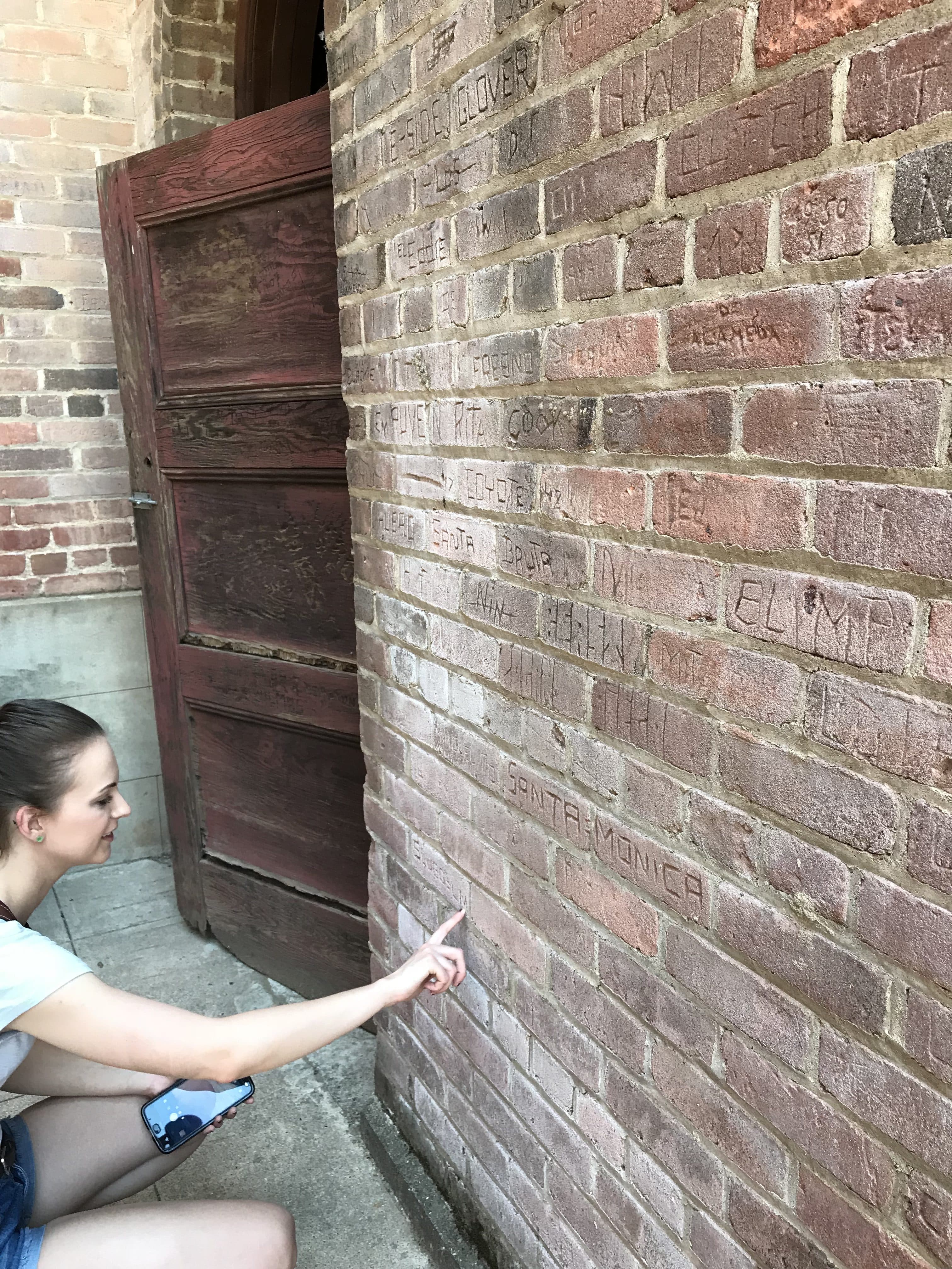 girl tracing her finger over names carved into a brick wall