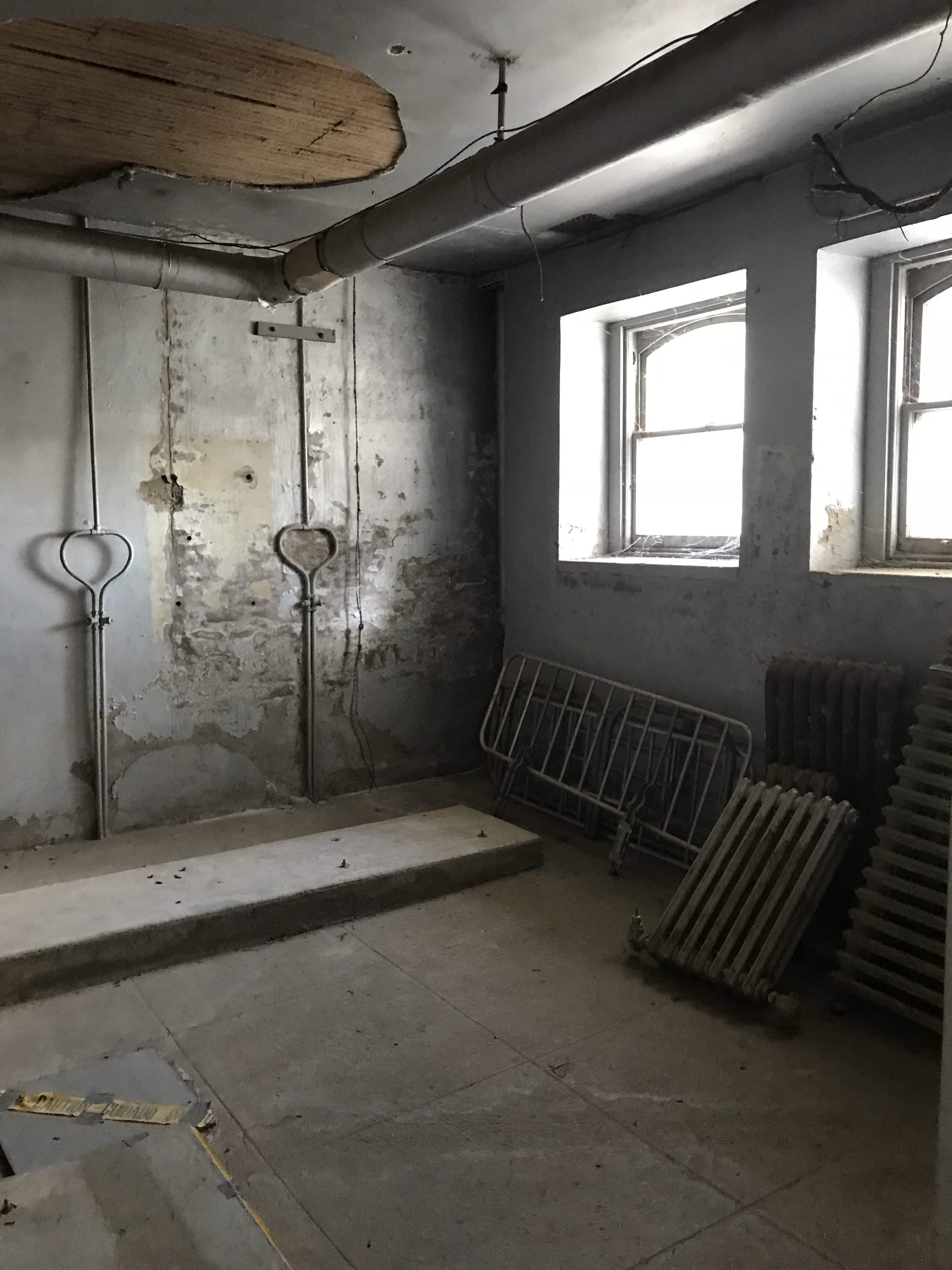 dark grey storage room with pipes, bedframes, and radiator parts