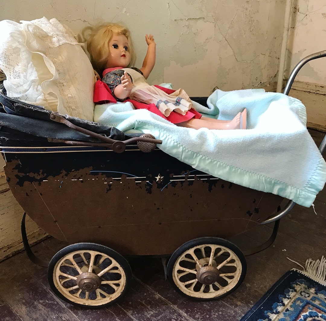 Antique doll in antique doll carriage in decaying room