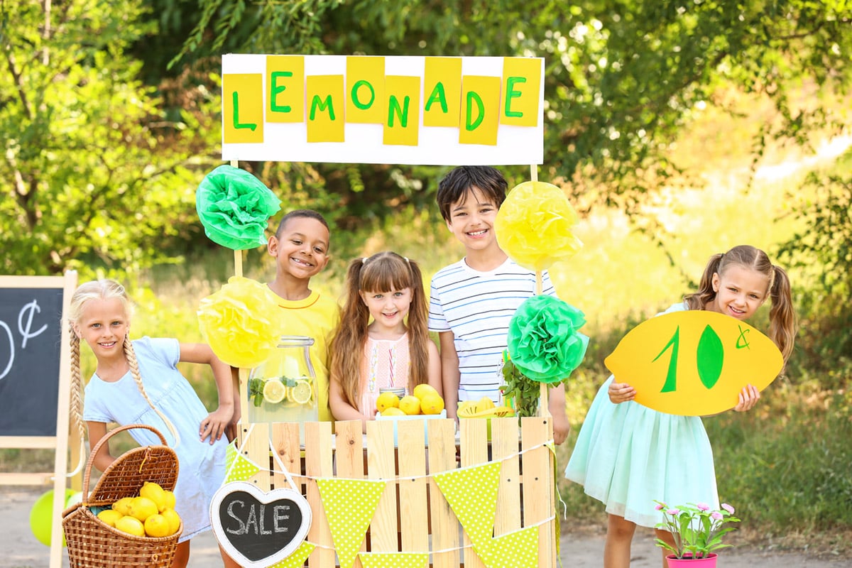 Five cute little children selling lemonade at lemonade stand in park