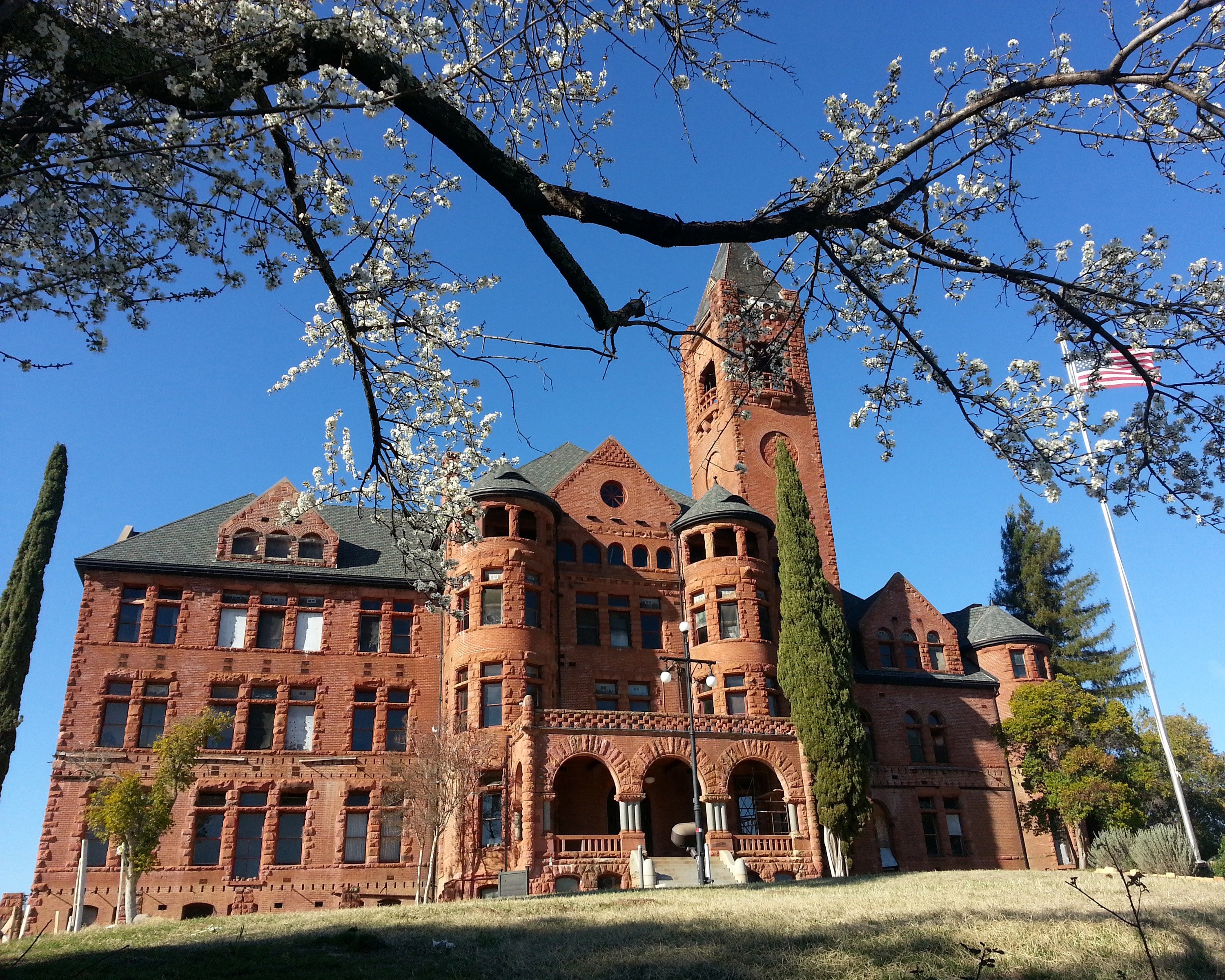 Preston Castle - large red brick building with clear blue sky, American flag, and blossoms on tree