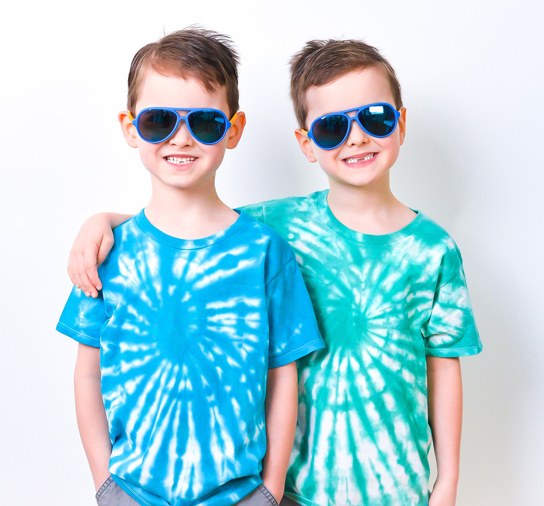 Twin 5-year-old boys wearing blue and green spiral tie-dye shirts and blue sunglasses