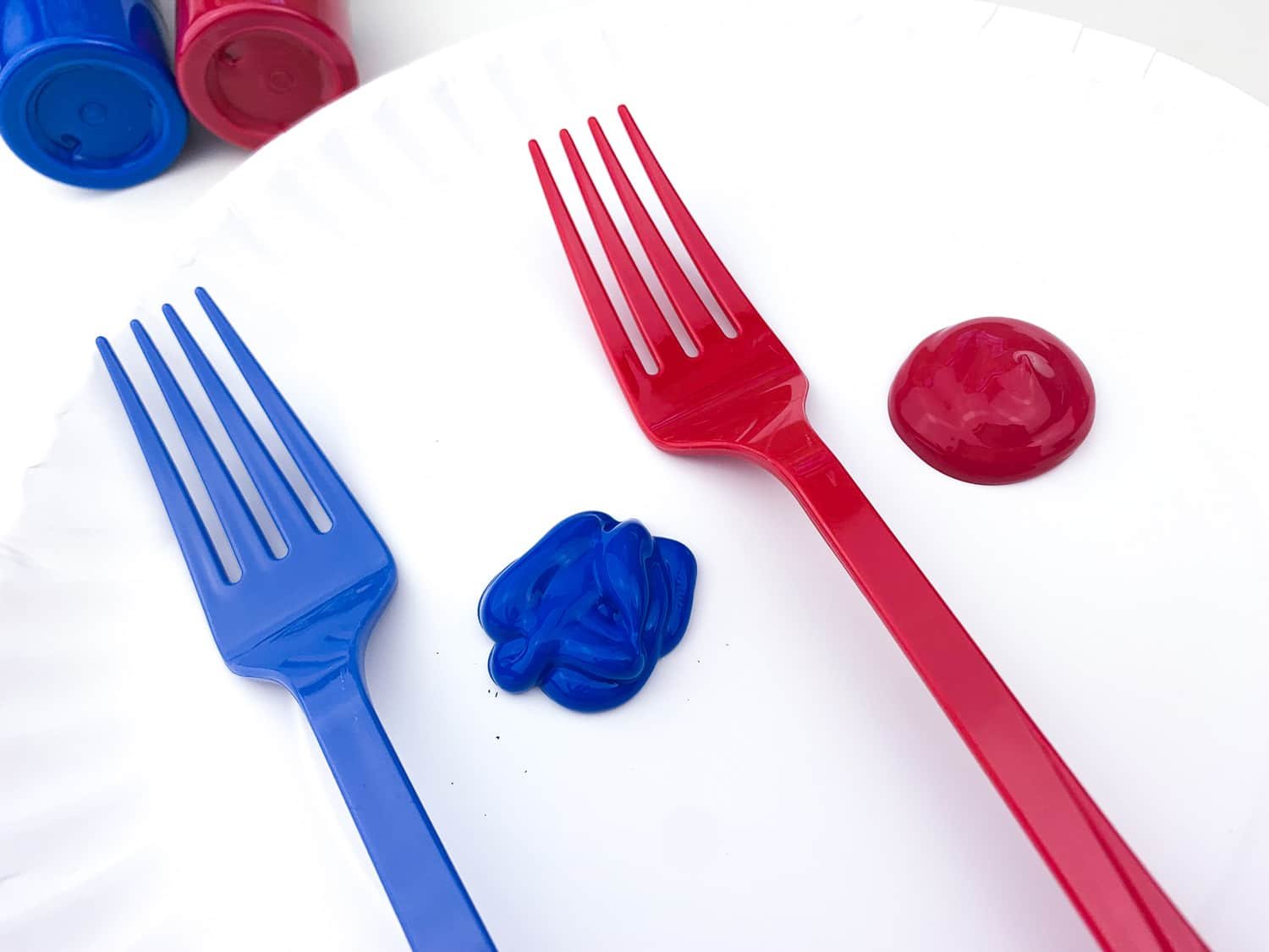 white paper plate with dots of blue and red paint, forks, and paint bottles