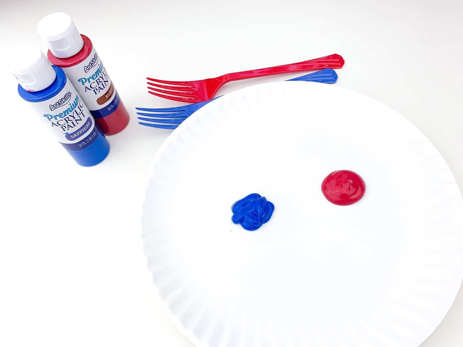 white paper plate with dots of blue and red paint, forks, and paint bottles