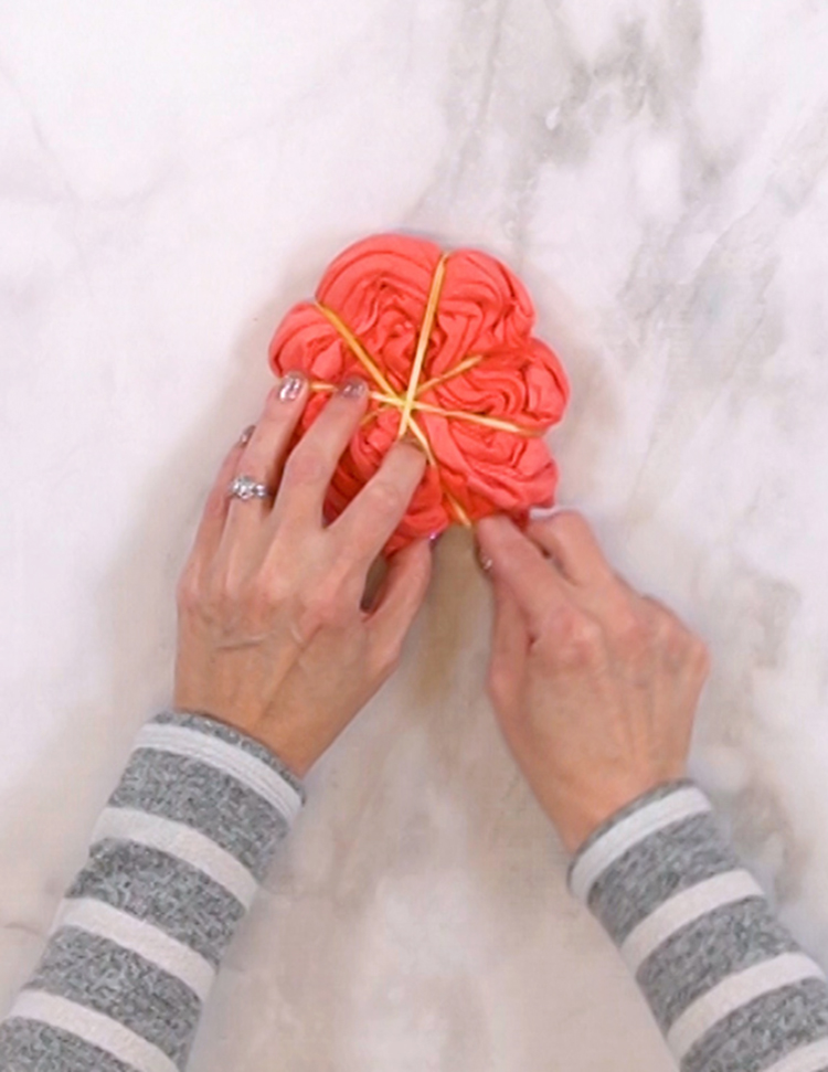 Hands folding a shirt into a spiral and securing with rubber bands