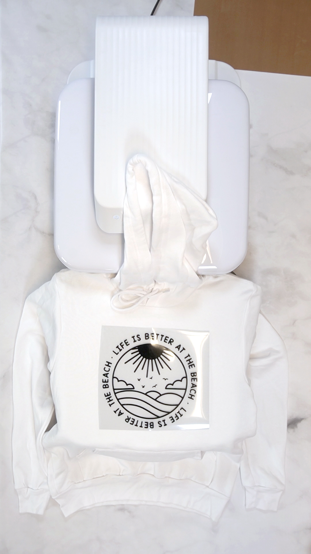 White hoodie on mat of HTVRONT Auto Heat Press with "life is better at the beach" graphic 