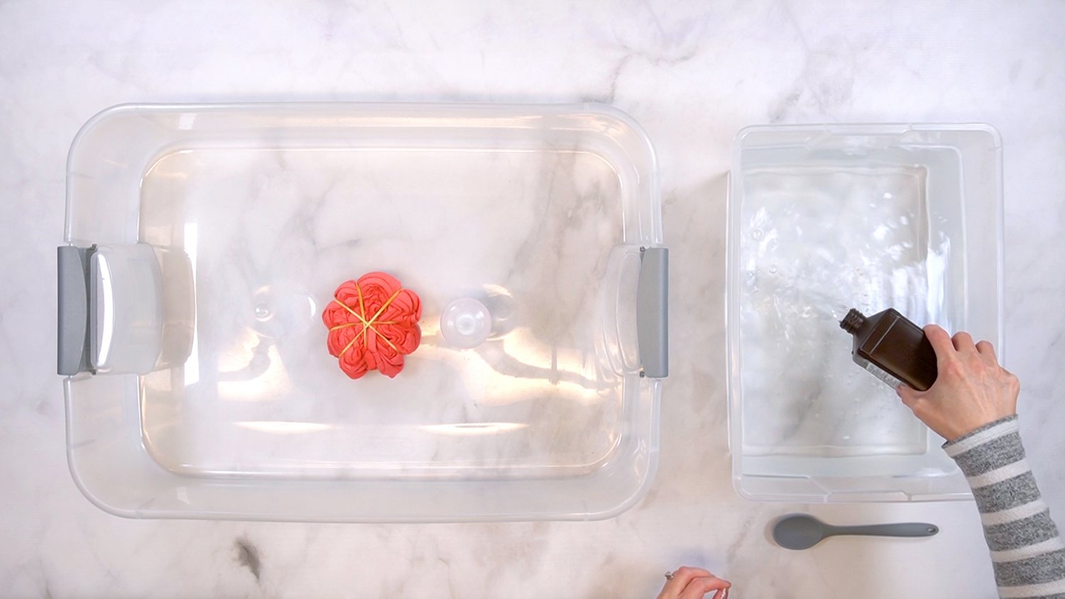 Overhead view of two plastic tubs on table, and hands mixing a bleach-neutralizing solution in the second tub