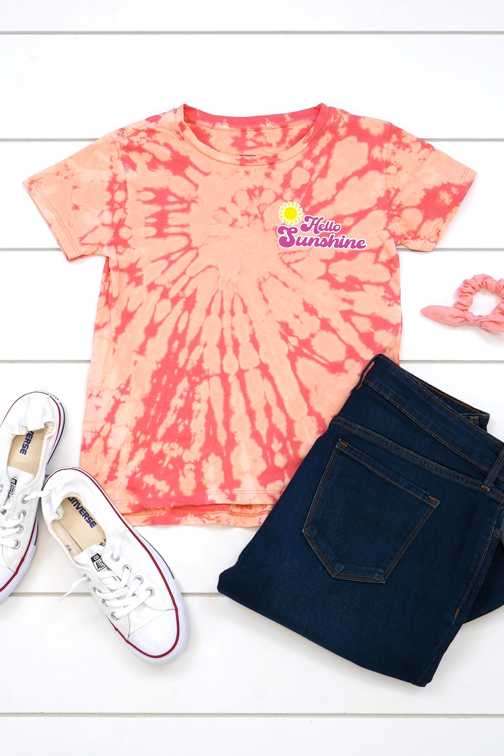 Peach and coral spiral bleach tie-dyed t-shirt with an outfit on white wood background