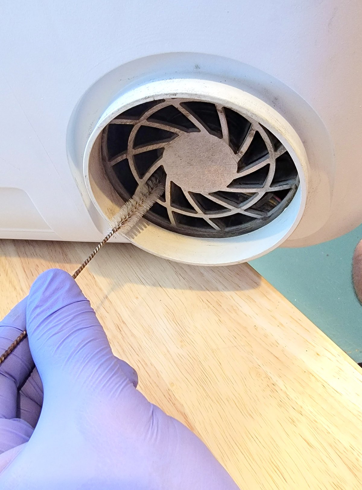 Close up of gloved hand cleaning a laser vent duct with a wire brush
