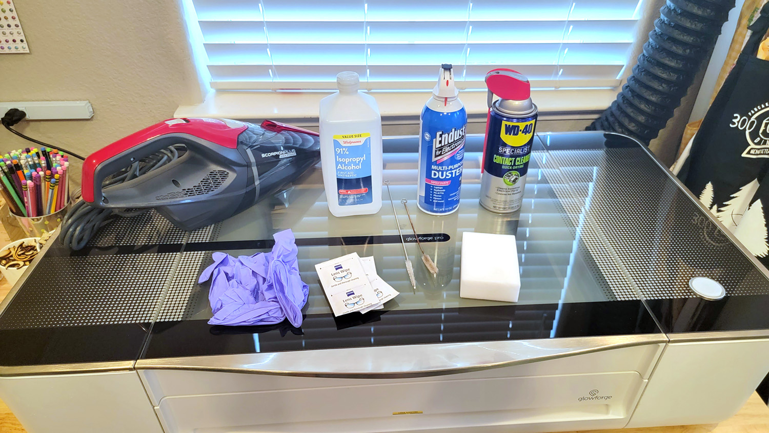 Cleaning supplies including isopropyl alcohol, gloves, and a mini vacuum on top of a Glowforge Pro machine