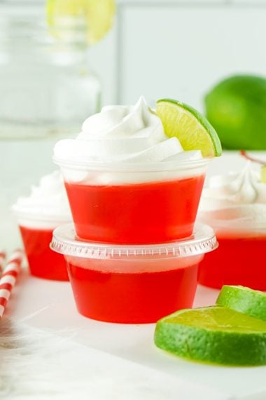 Close up of two stacked red jello shots with whipped cream and a lime wedge