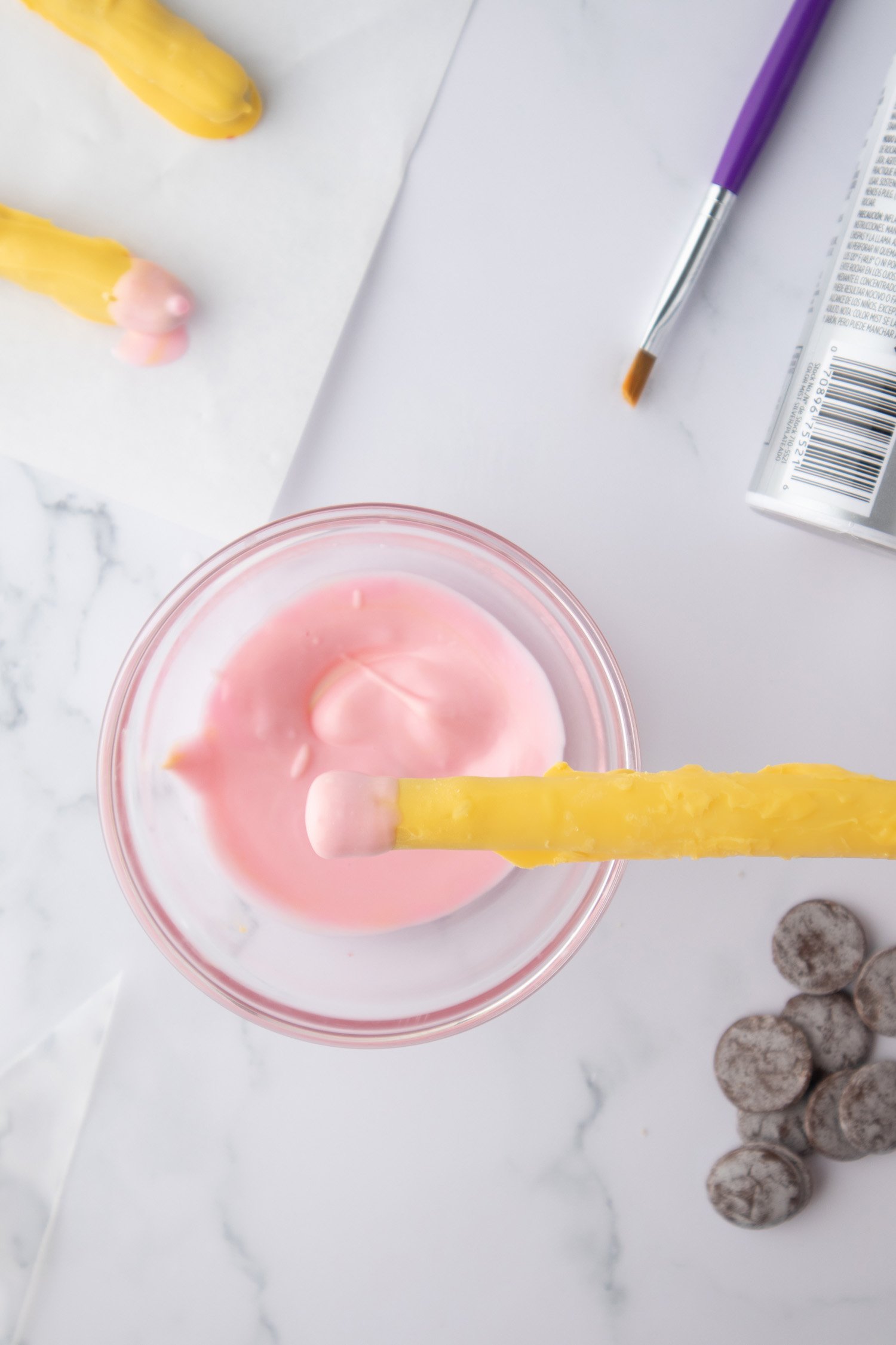 dipping yellow pencil snack end into pink melted chocolate