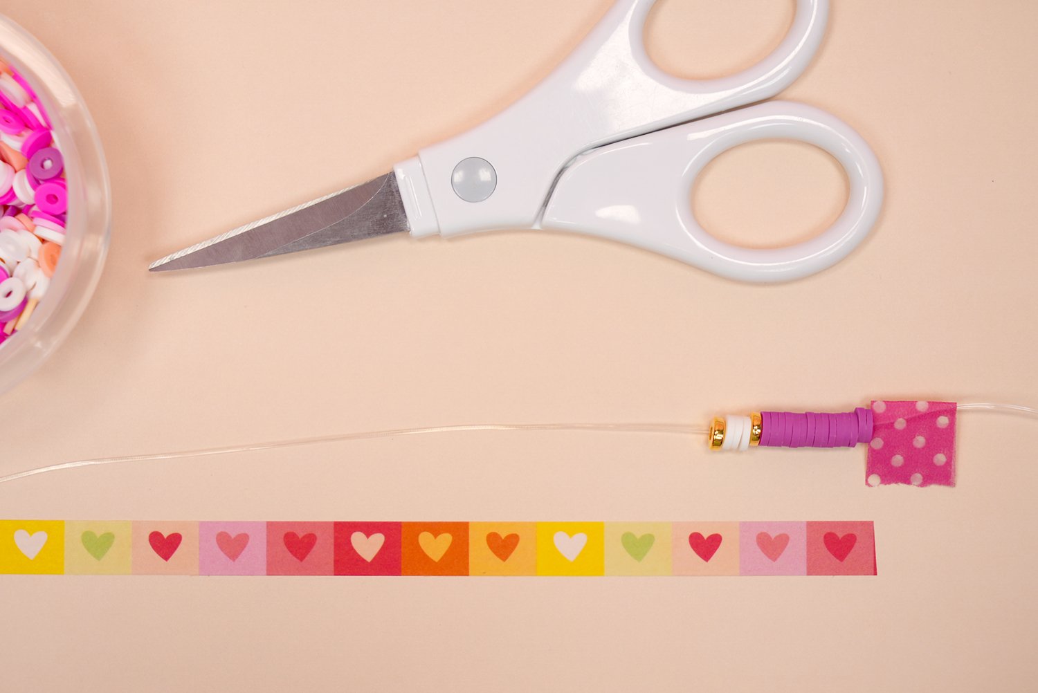 Close up of beads on a string in color block pattern with scissors and measuring washi tape