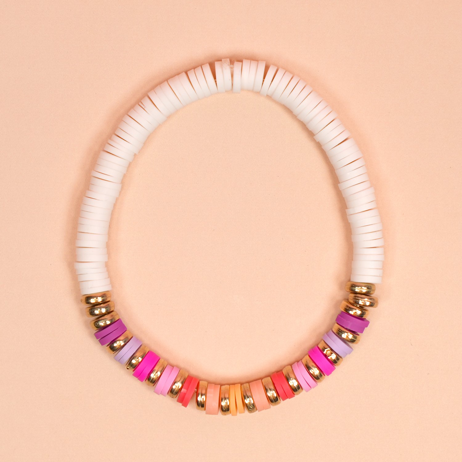 White clay bead bracelet with colorful bead and gold disc accents on peach background