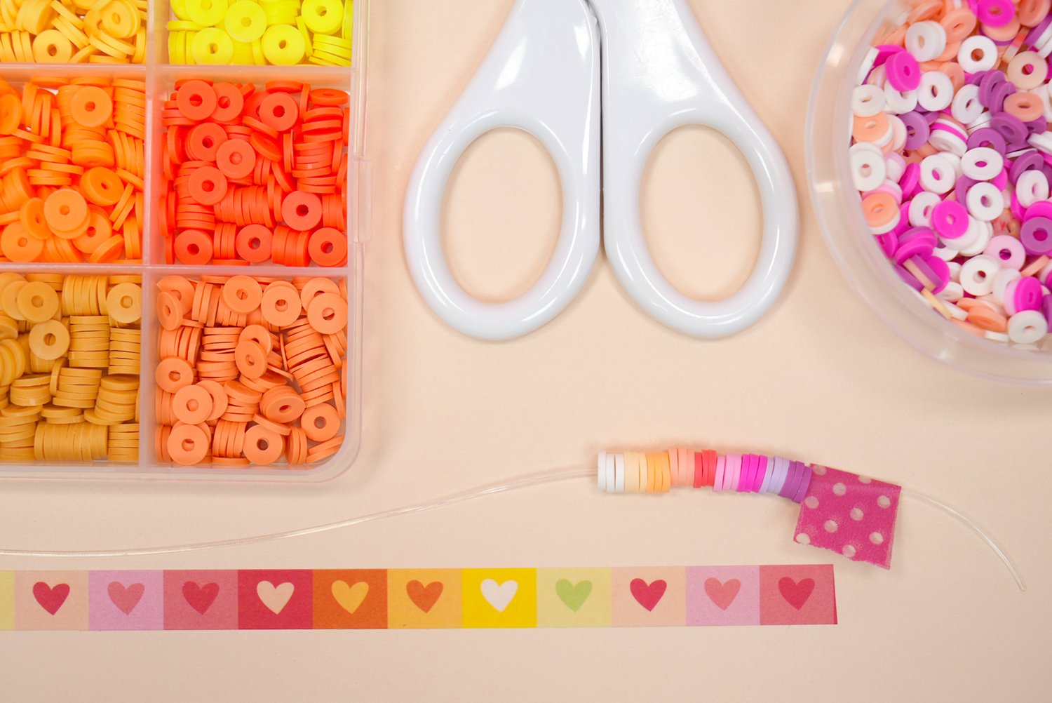 Close up of beads on a string in ombre sunset pattern with scissors and measuring washi tape