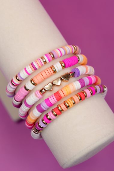 Five colorful heishi clay beaded bracelets on a cream display stand with purple background