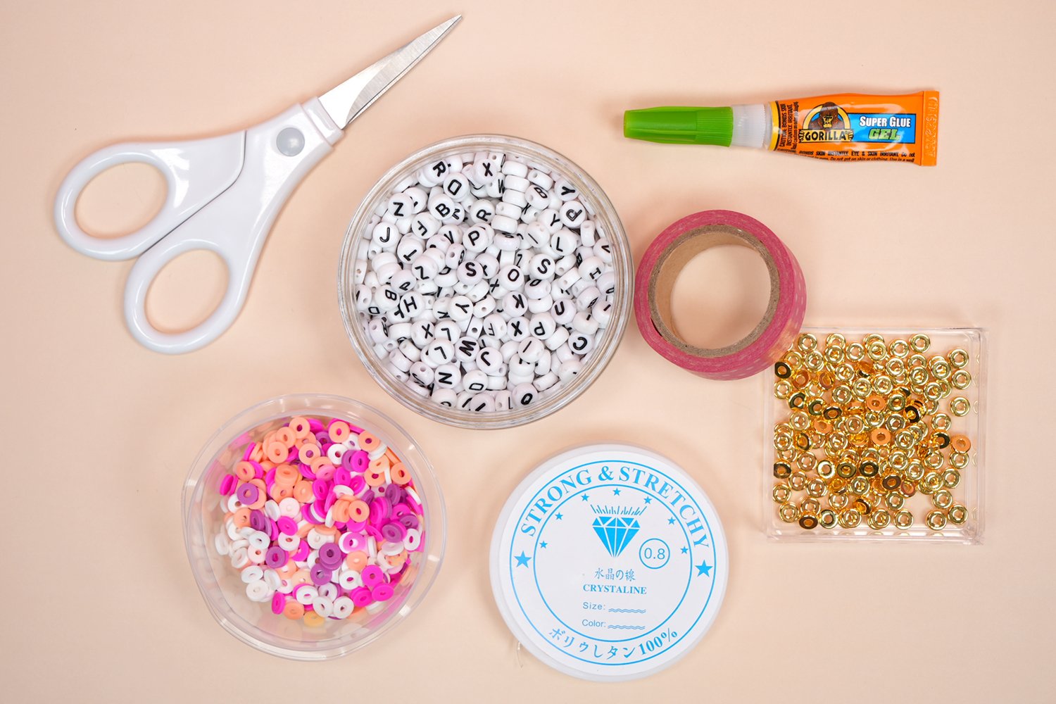 Supplies for making clay bead bracelets - clay beads, alphabet beads, spacers, string, scissors, etc. on peach background