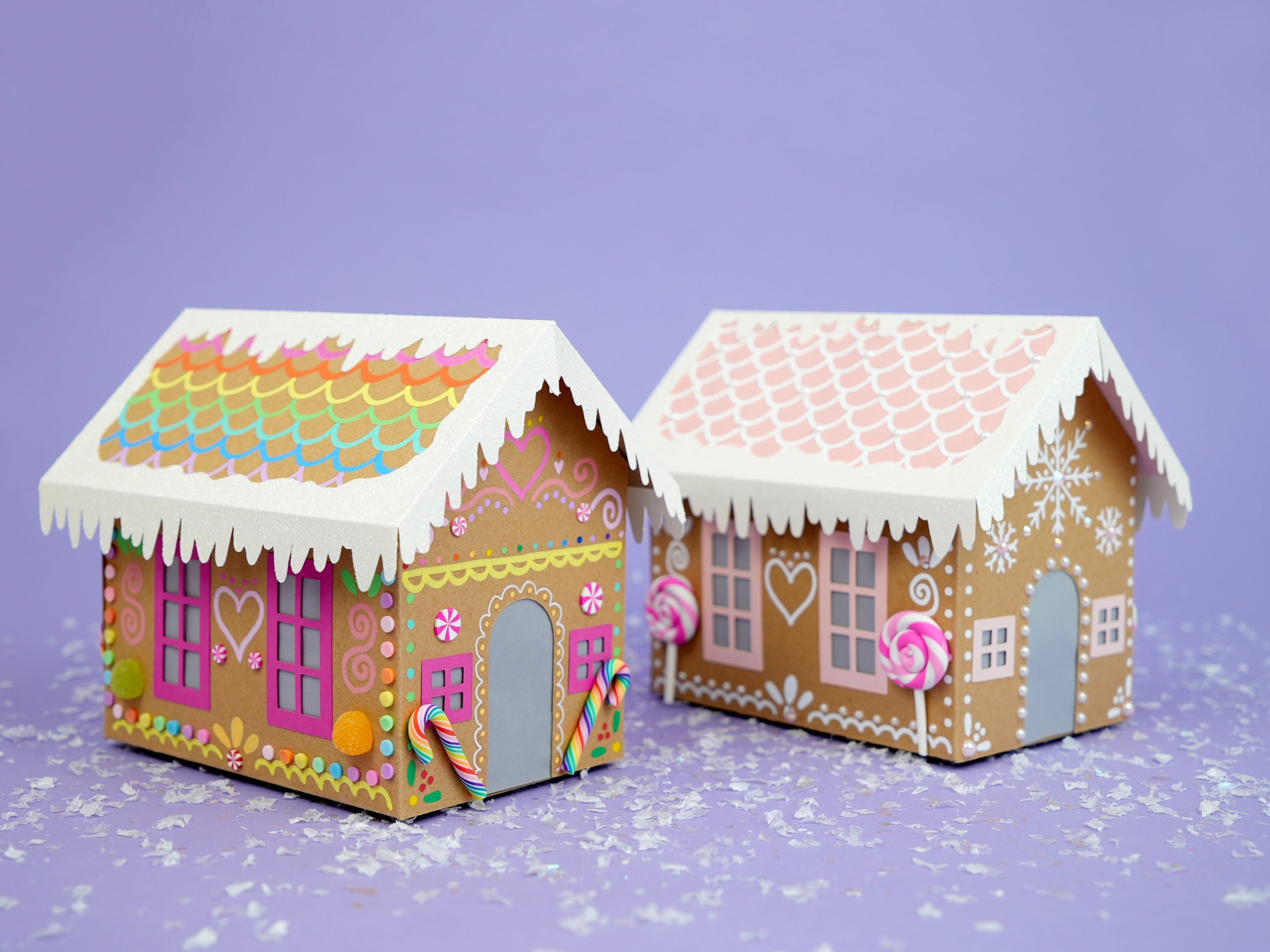 Two decorated paper gingerbread house on lavender background with faux snow