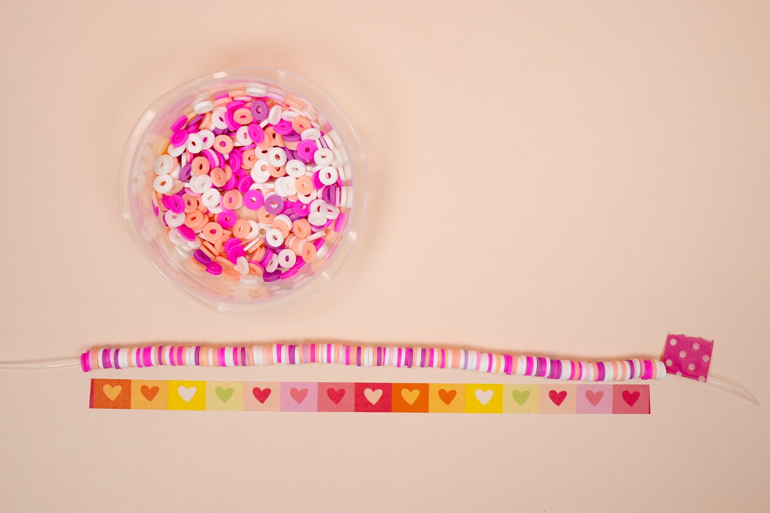 String of clay beads being measured against a 7" strip of washi tape for length on peach background