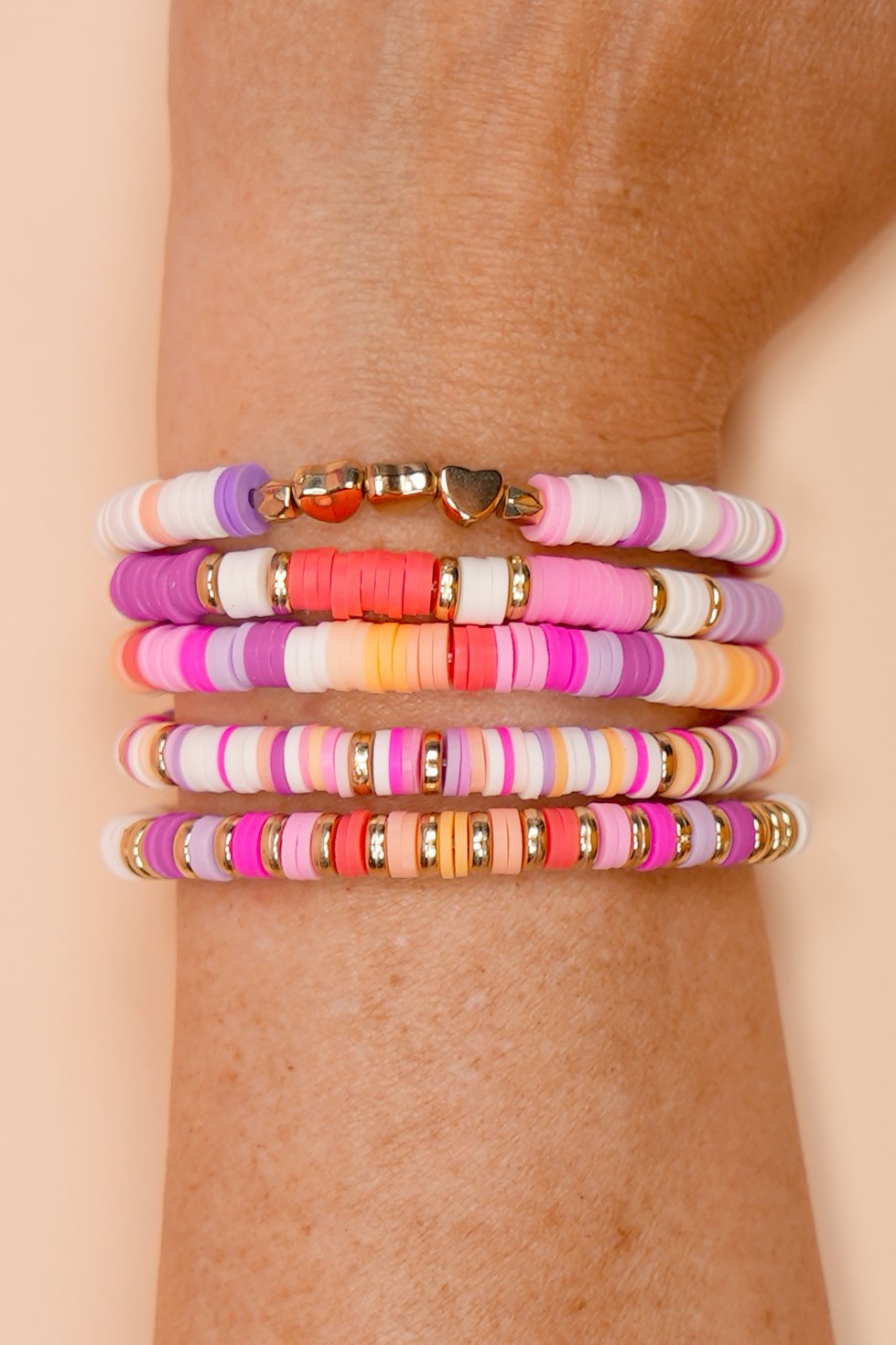 Close up of wrist with five colorful preppy clay bead bracelets in a sunset color palette
