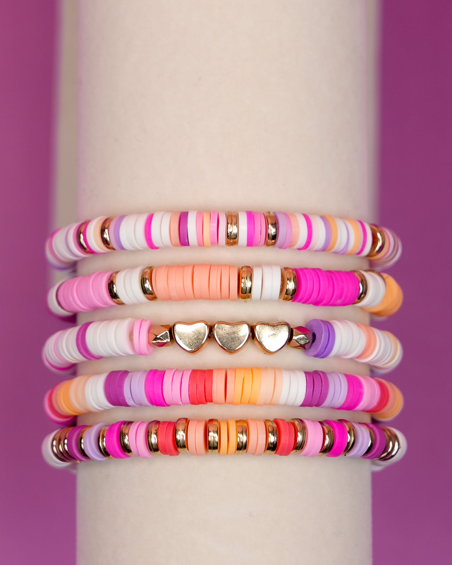 Close up of heishi clay bead bracelets - colorful preppy clay bead bracelet set on display stand on purple background