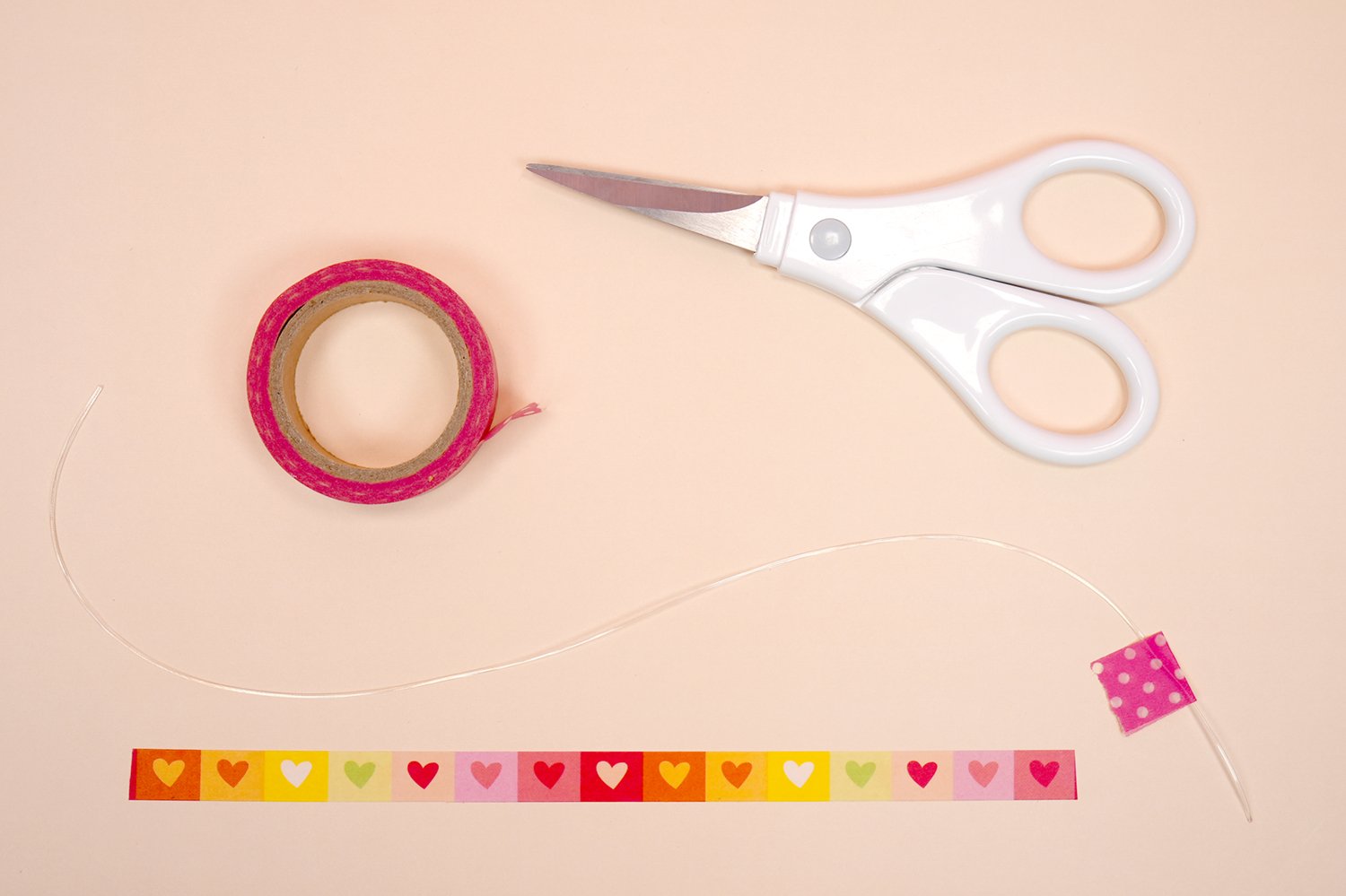 Stretchy bracelet cord with a piece of washi tape at end, next to a roll of washi tape and scissors