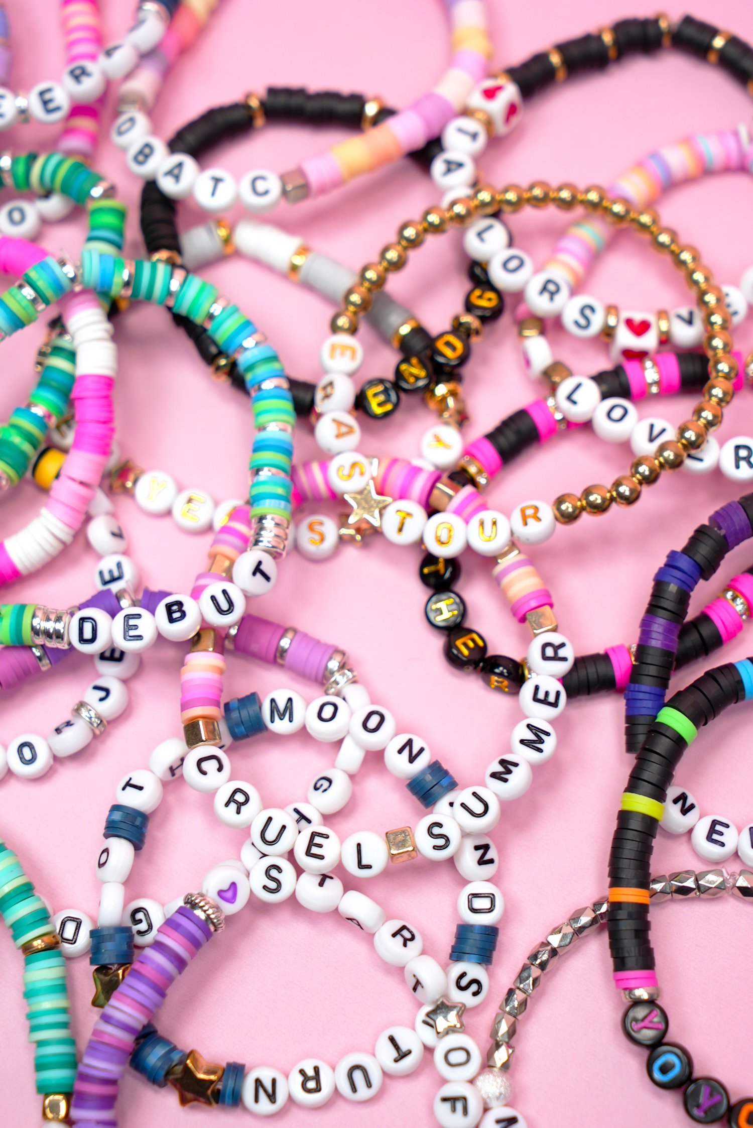 Colorful beaded Taylor Swift friendship bracelets for the Eras Tour on a pink background