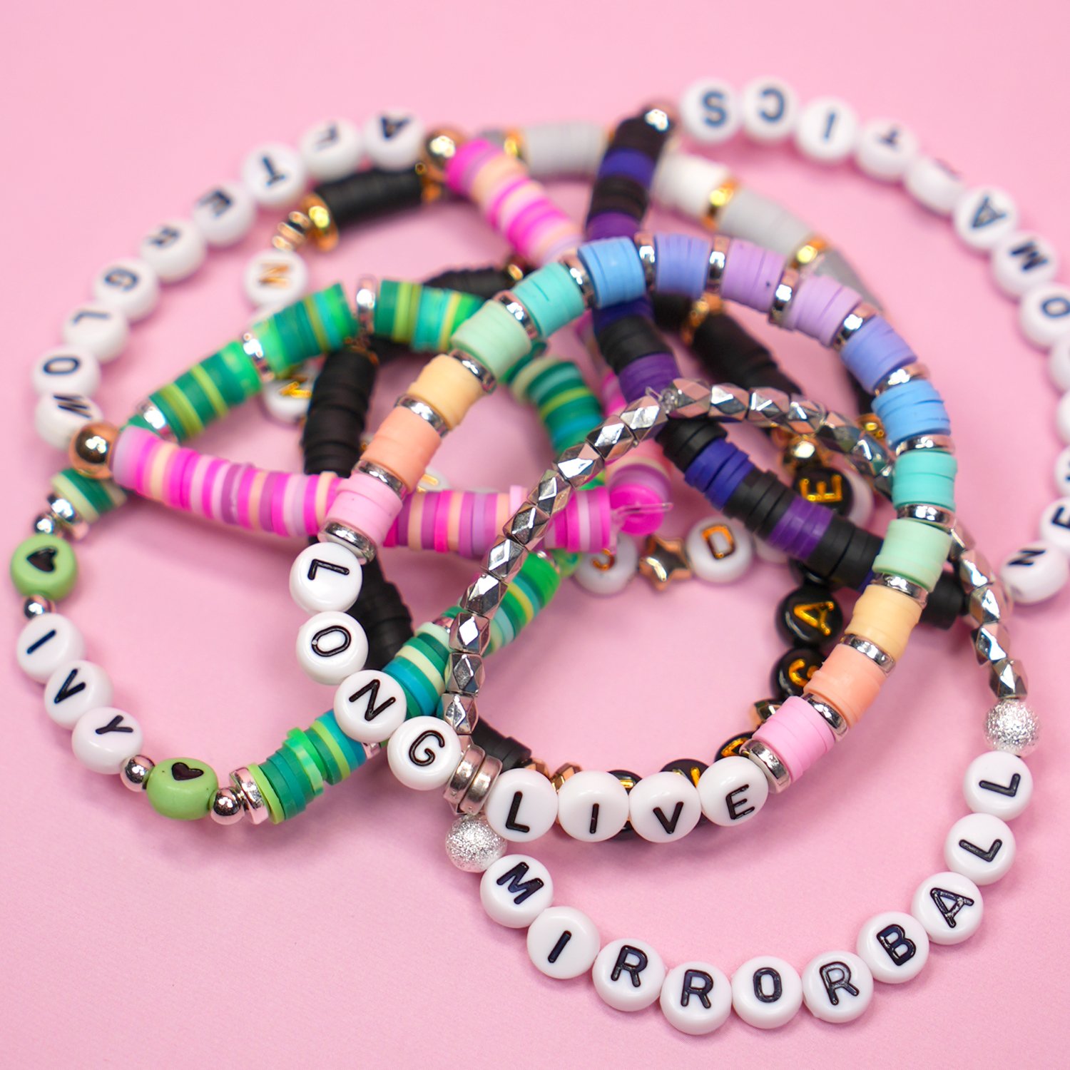 Stack of colorful beaded bracelets featuring Taylor Swift song titles on pink background