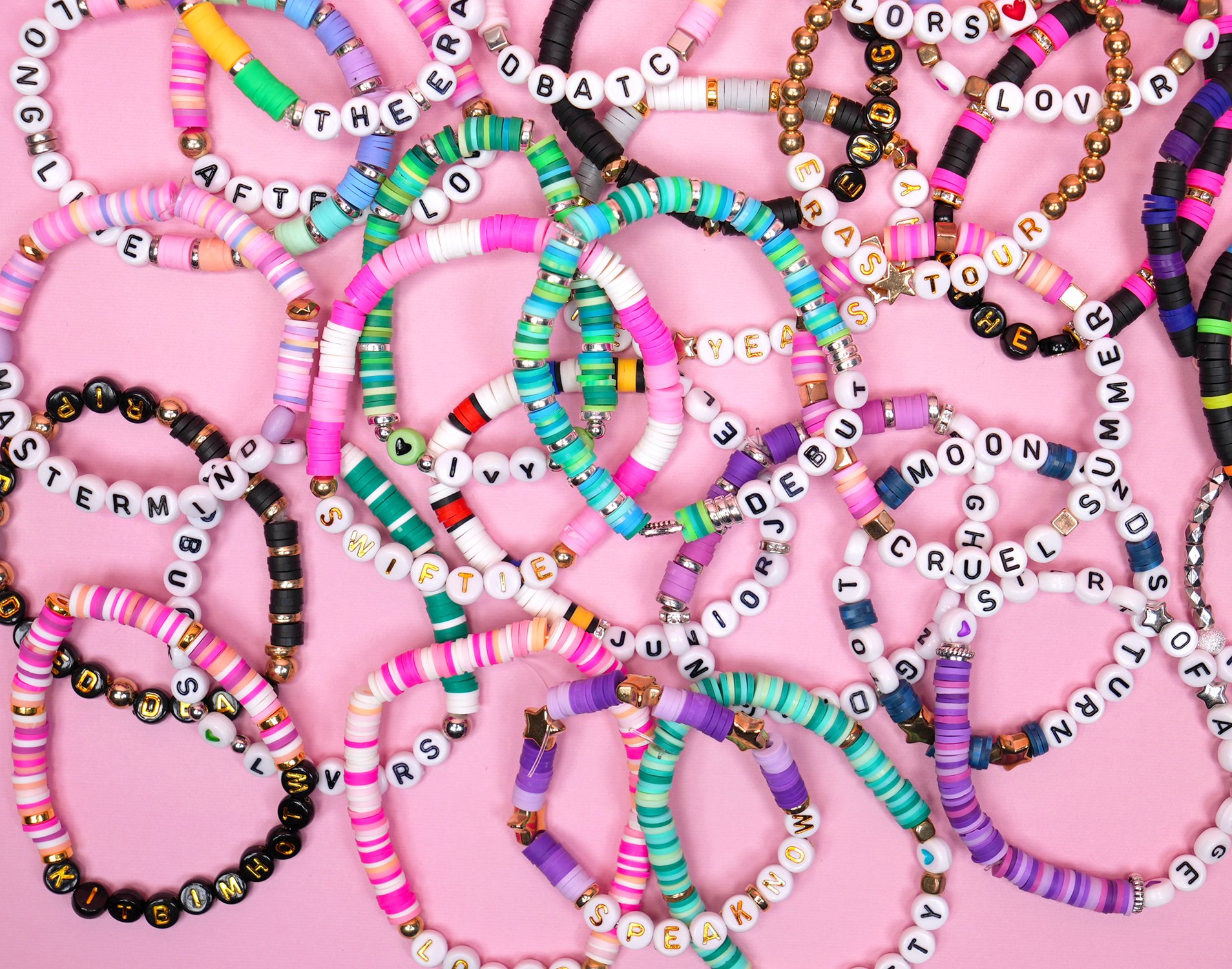 Pile of many colorful beaded Taylor Swift Eras Tour friendship bracelets on a pink background