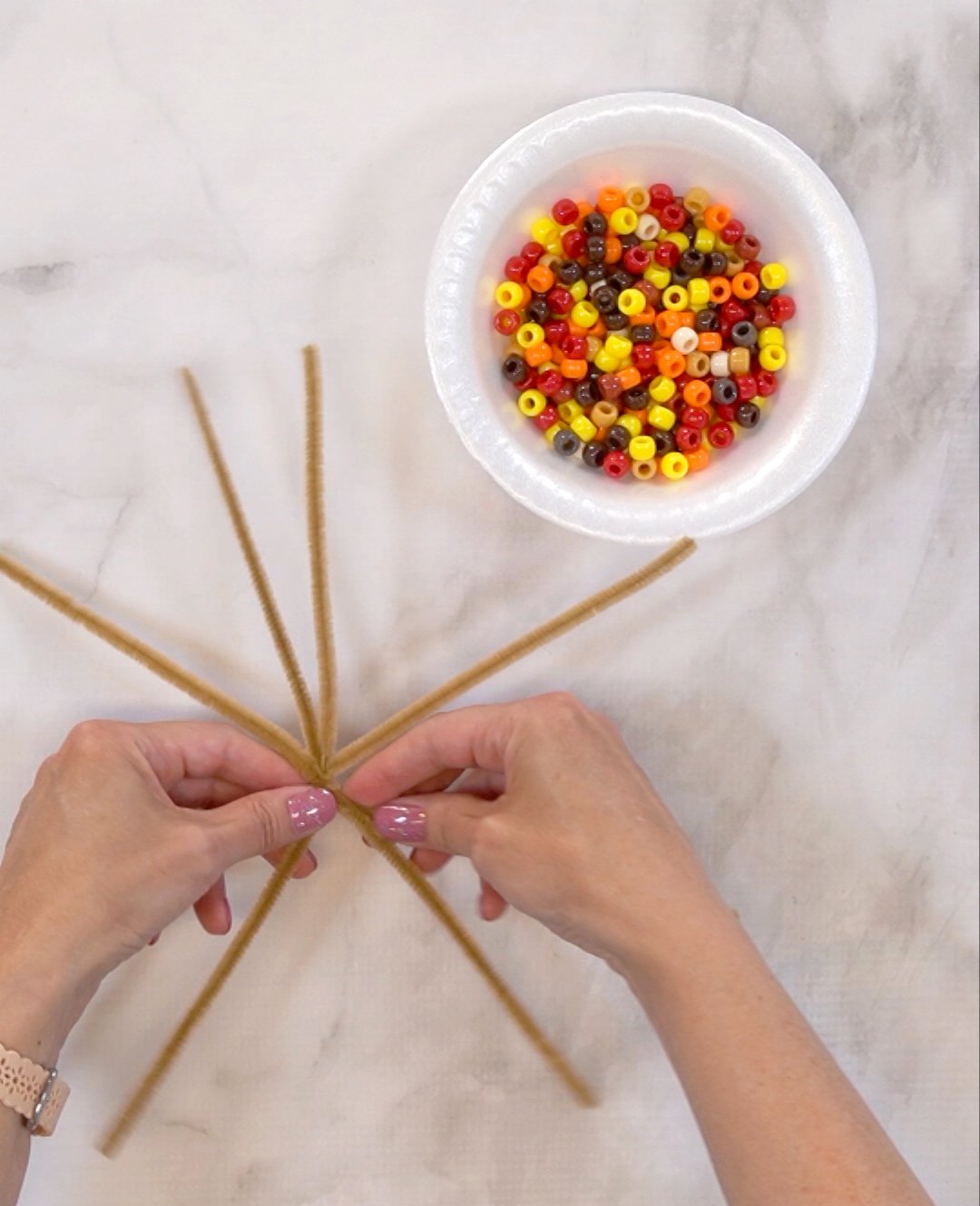 hands twisting together pipe cleaners with bowl of beads nearby