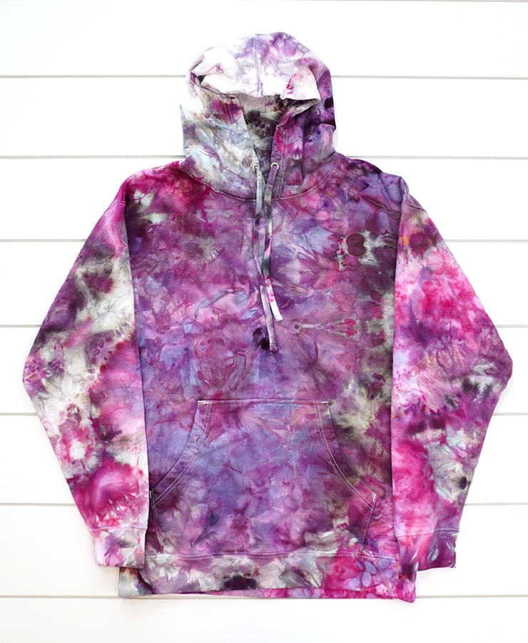 Ice dyed hoodie in assorted shades of color including pink, purple, and grey on white wood background