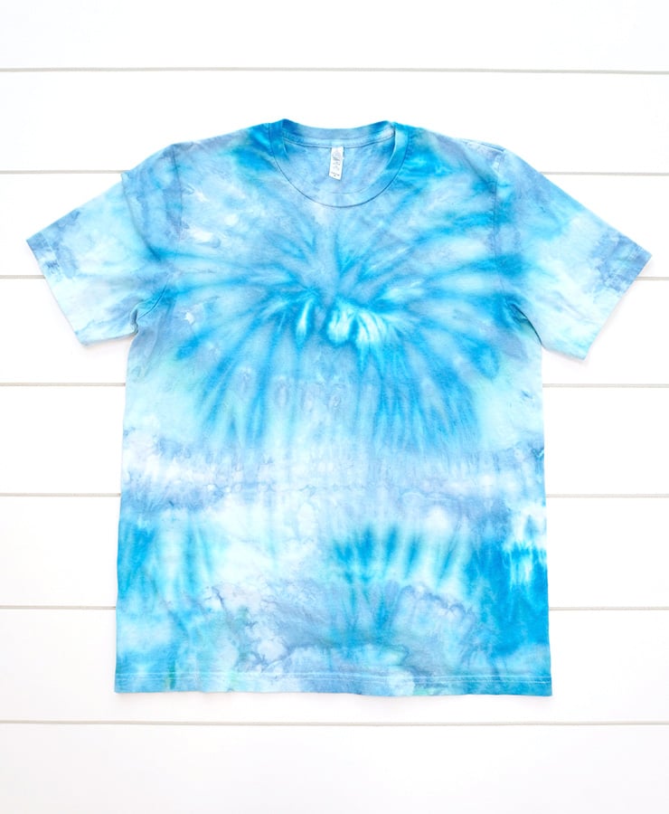 Light blue ice dyed t-shirt on white wood background, looking slightly faded