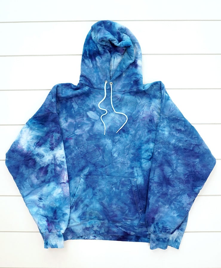 Ice dyed white fabric hoodie in many shades of blue on white wood background
