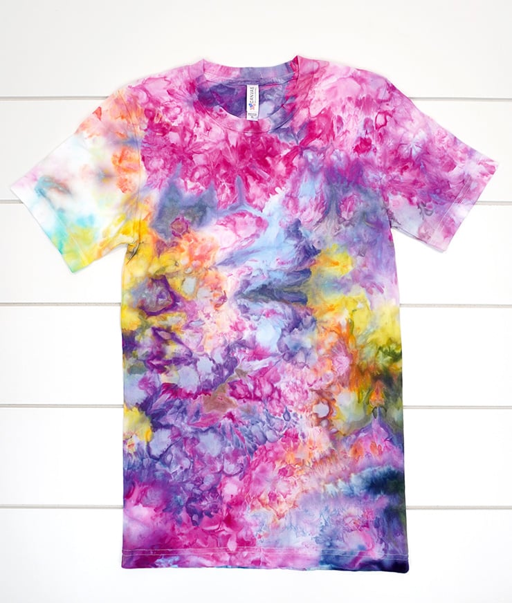 Ice dyed shirt on white wood background with all the colors of the rainbow, resulting in a few "muddy" spots of color