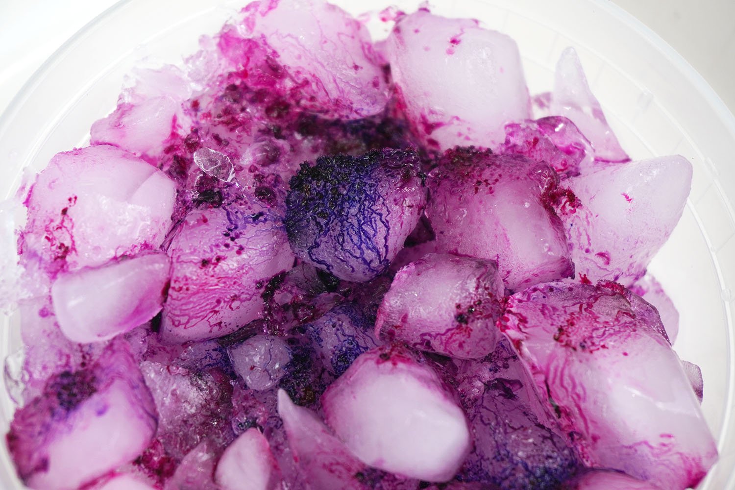 Close up of fuchsia dye splitting into blue and pink colors on ice