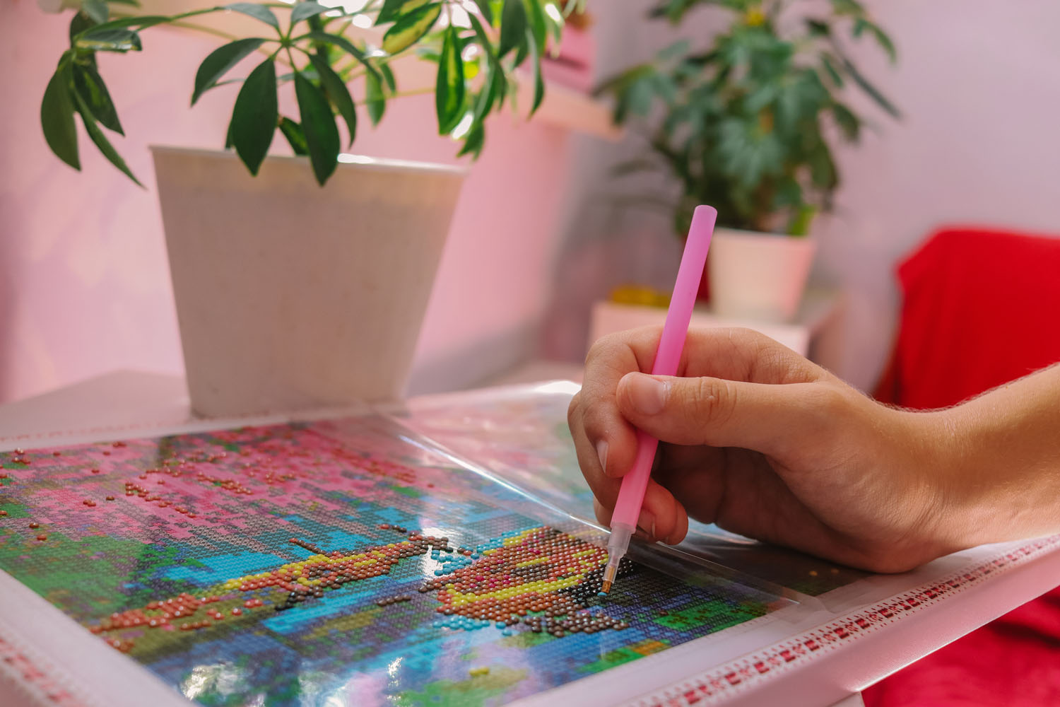 Close up of hand with pink diamond paint pen working to create a diamond painting