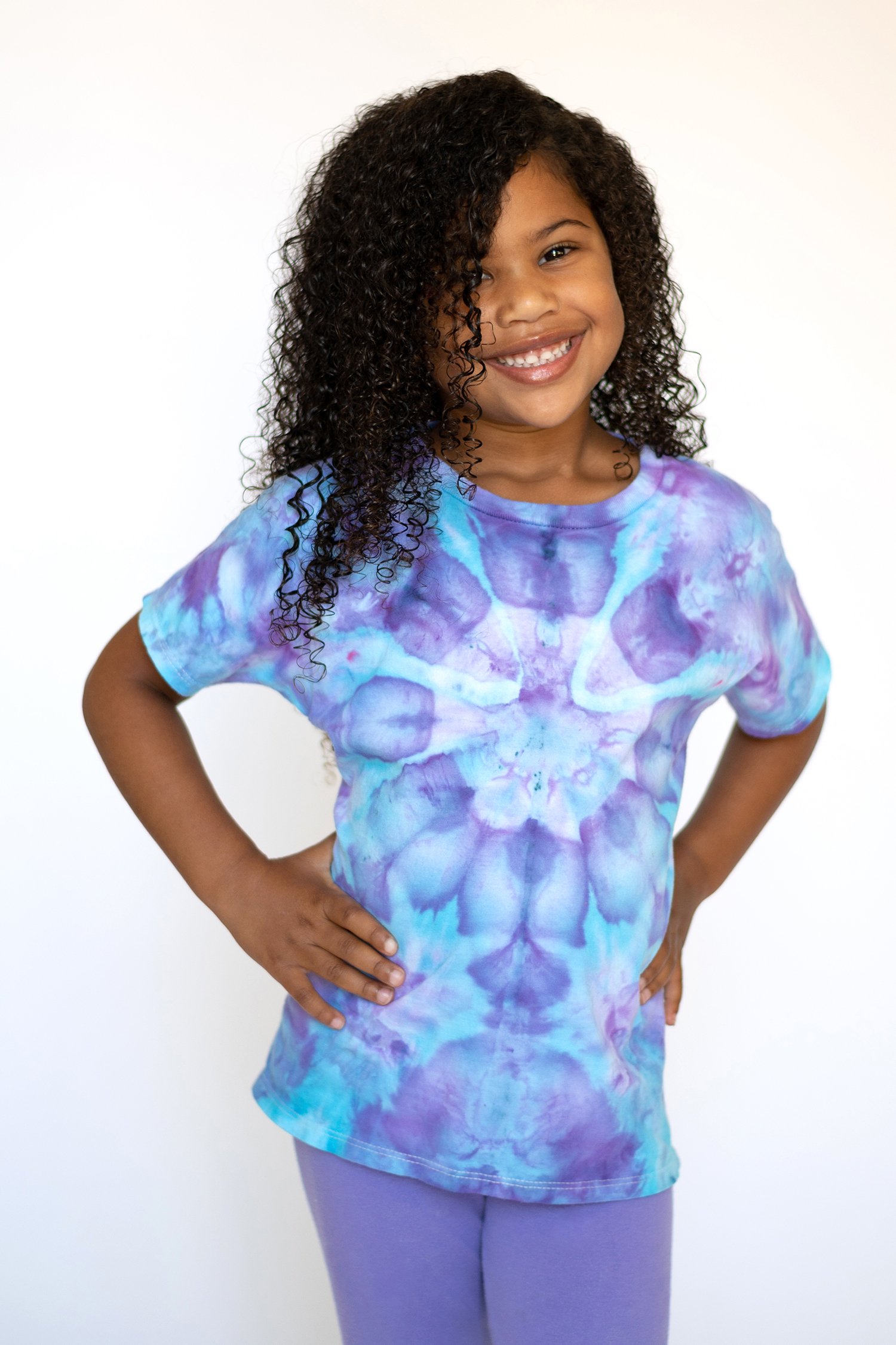 Cute smiling young Black girl with curly hair wearing a purple and blue ice dyed t-shirt 