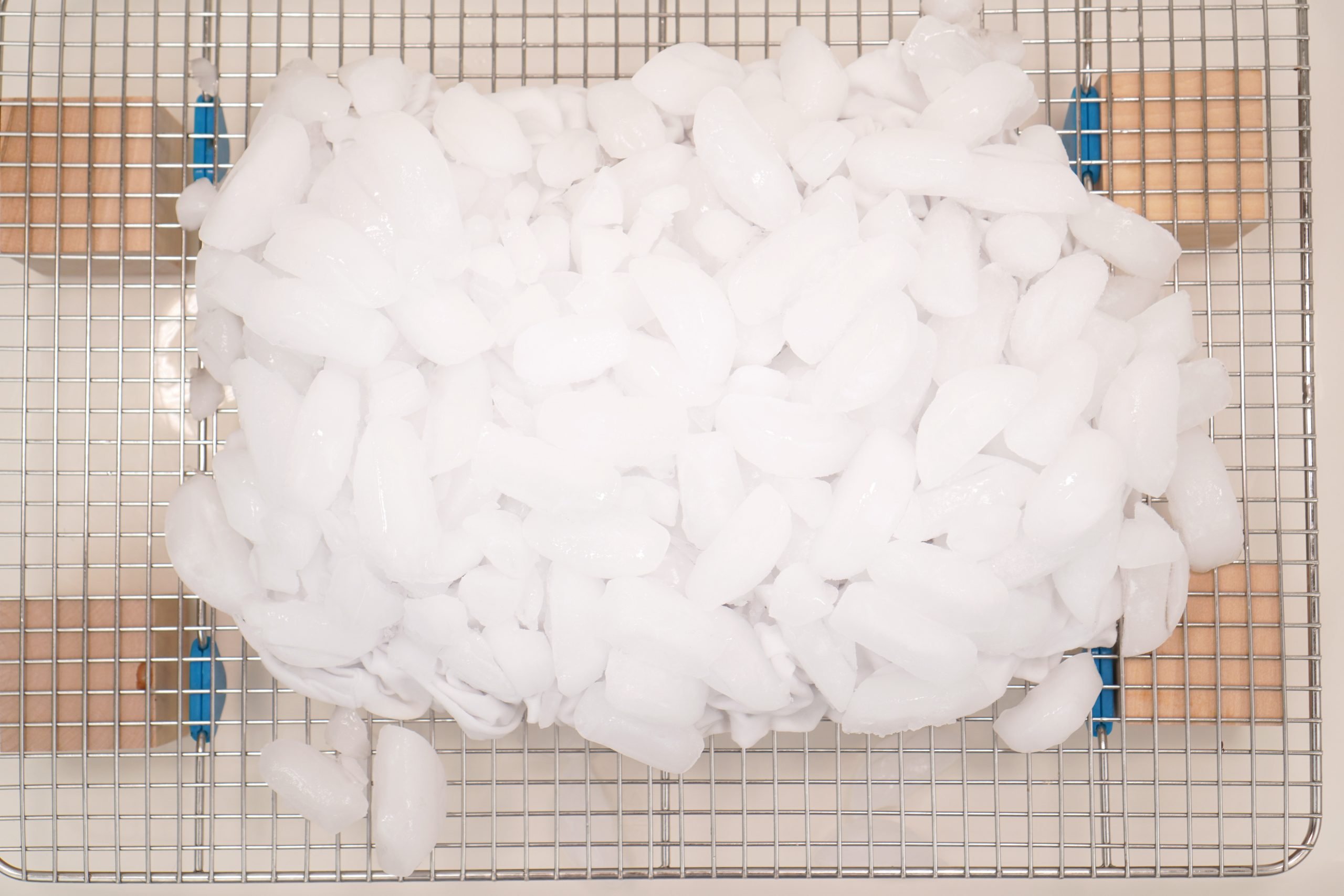 crumpled fabric covered in a layer of ice atop a wire rack in bottom of plastic tub in preparation for ice dye