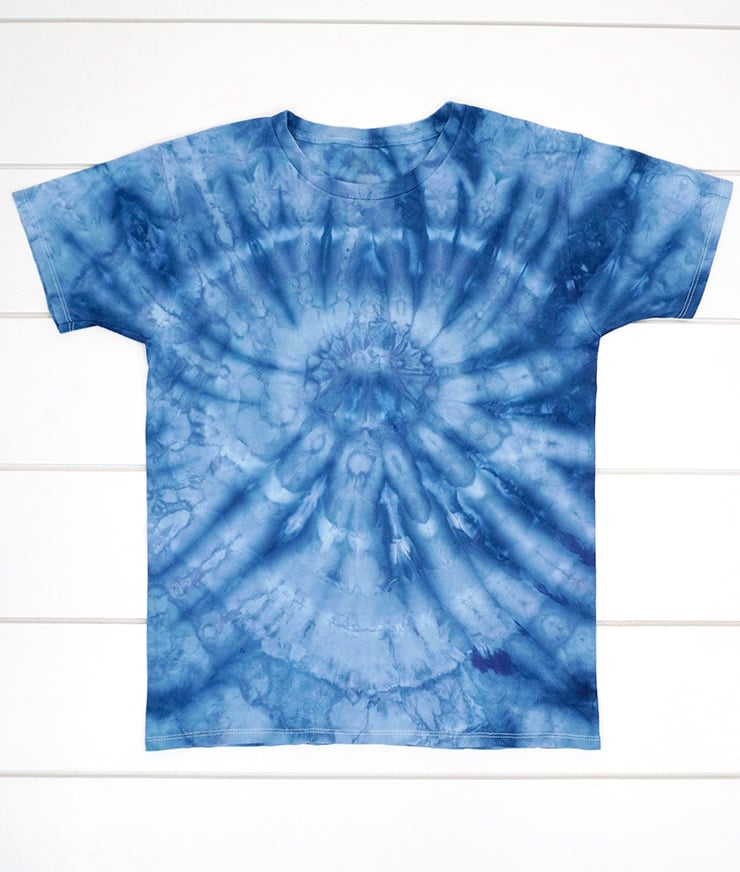 Ice dye shirt with "spider" folding pattern in shades of dark blue on white wood background