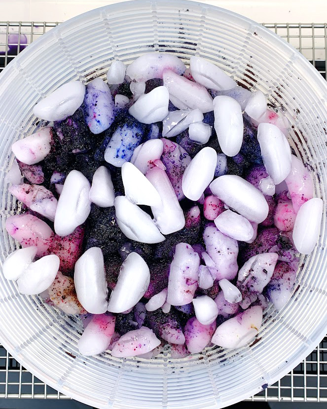 Partially melted ice with blue and purple dye on top of an ice dye t-shirt inside a salad spinner basket