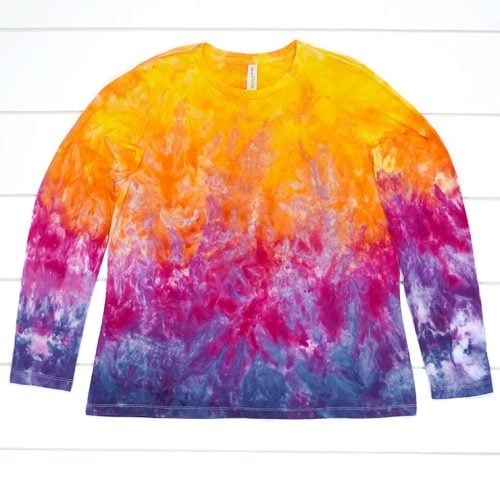 Ice dyed long sleeve t-shirt in sunset shades of yellow, orange, pink, purple, and navy blue on white wood background