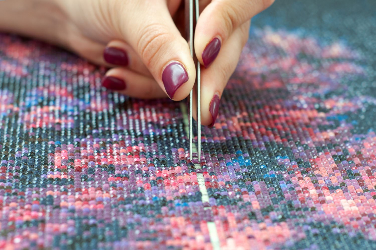 Close up of female hand creating diamond embroidery painting with tweezers and acrylic rhinestones