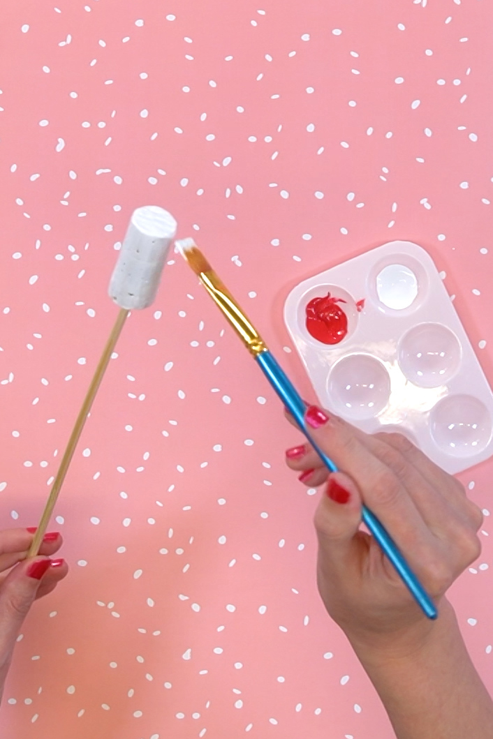 hands painting a wine cork on a skewer with paint in background