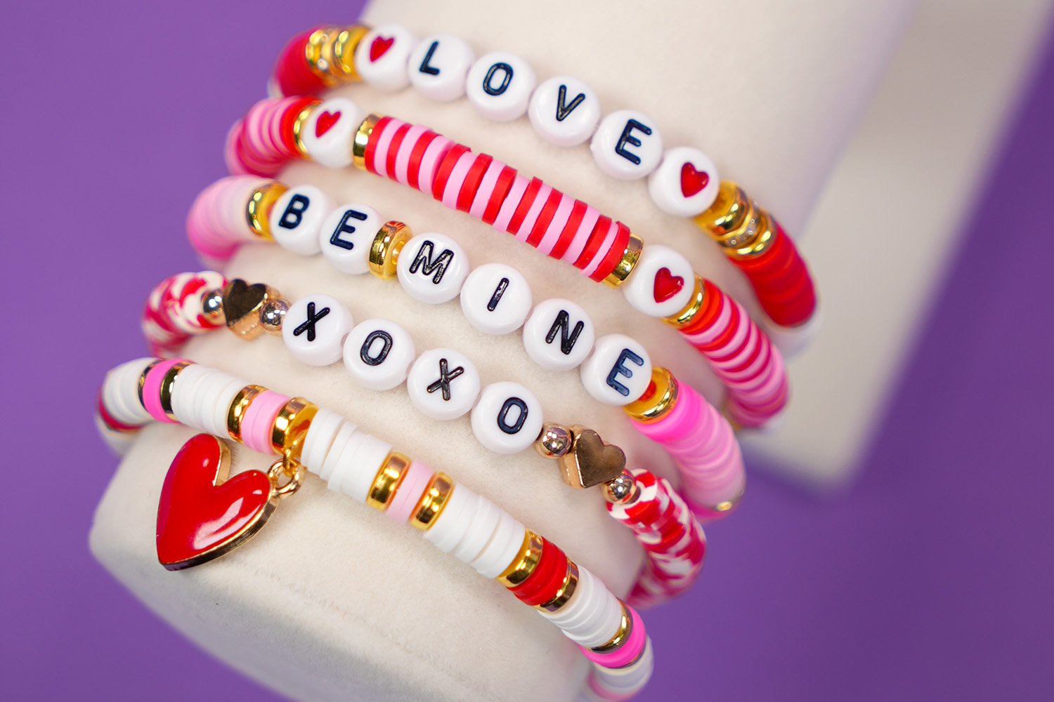 Close up of Valentine's Day bracelets with pink, red, and white beads and "LOVE," "BE MINE," and "XOXO" beads