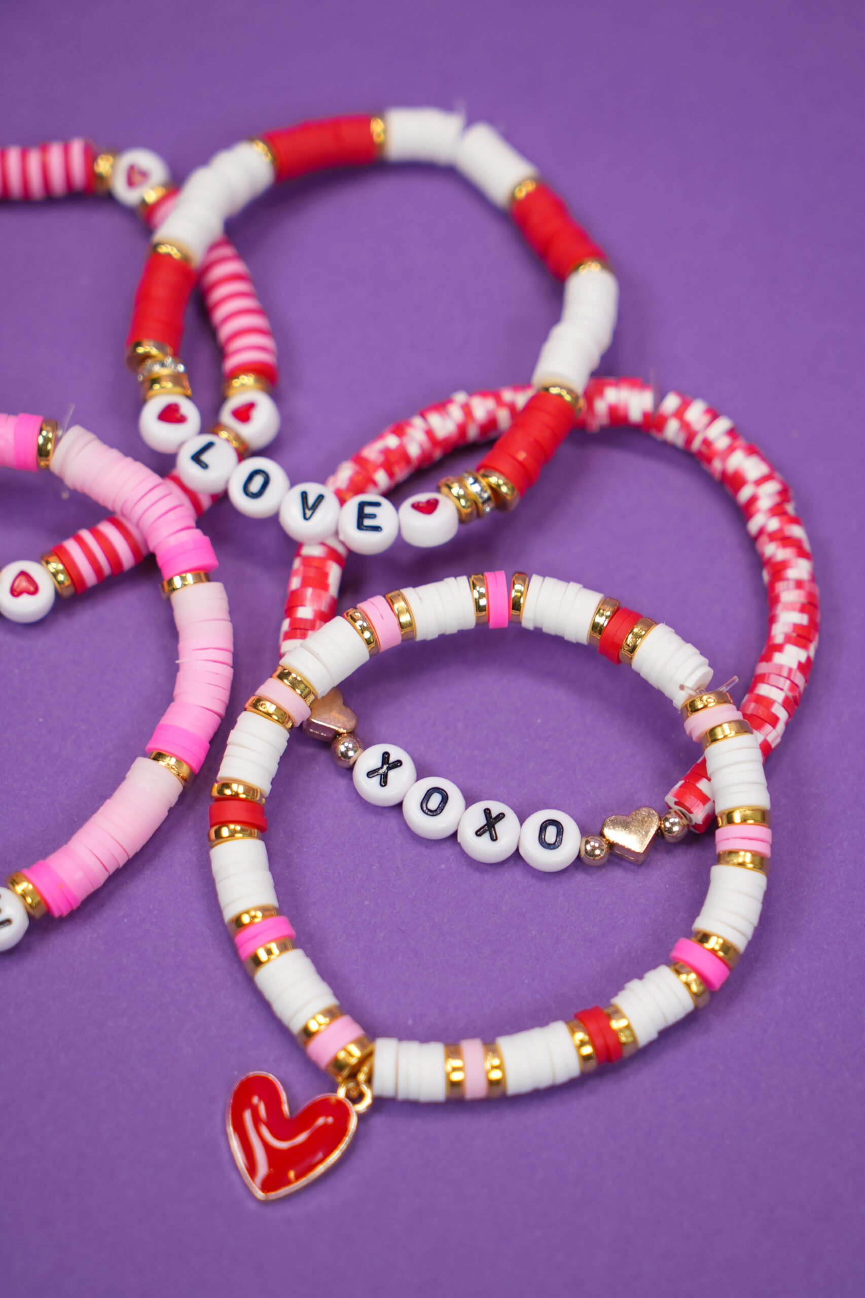 Stacked clay bead bracelets with Valentine's Day colors and theme on purple background