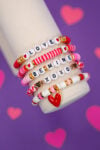 Close up of Valentine's Day bracelet set with red, pink, and white beads on display arm on purple background