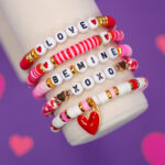 Close up of Valentine's Day bracelet set with red, pink, and white beads on display arm on purple background